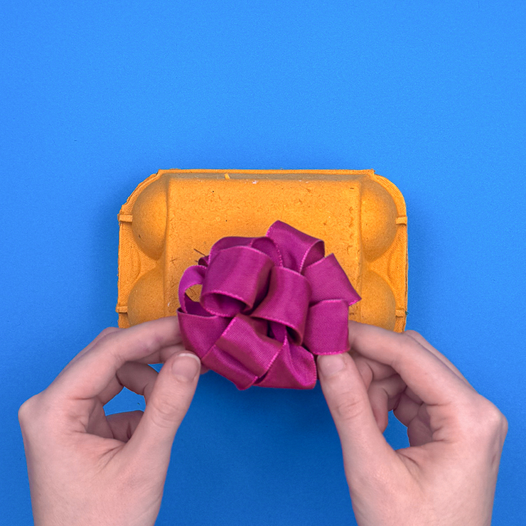 Ein Bild das zeigt, wie zum Schluss eine Schleife auf den Karton gebunden wird.