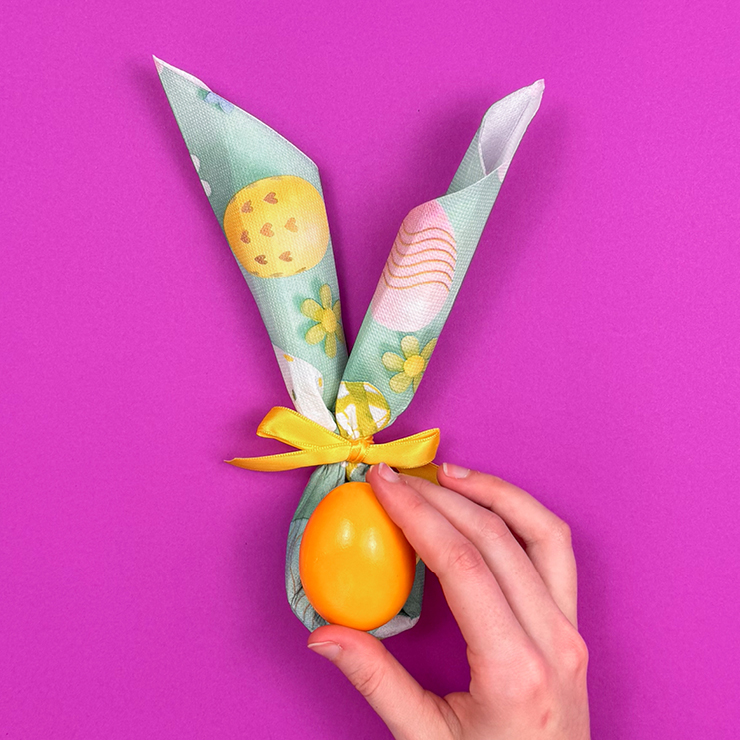 Ein Bild das zeigt, wie ein Osterei in die Öffnung der Serviette gelegt wird.