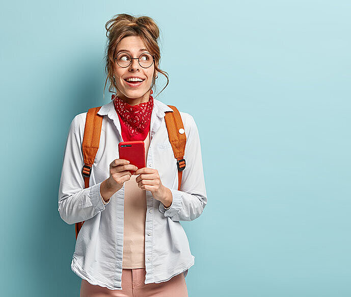 Lotto Reklamationsfrist Ein junge Frau ist mit ihrem Handy in der Hand vor einer hellblauen Wand abgebildet